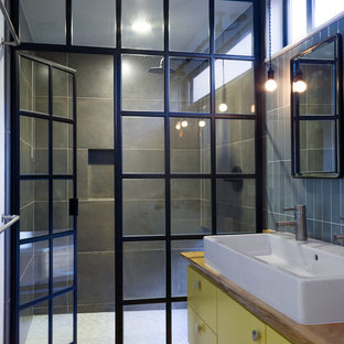 Modelo de cuarto de baño urbano con lavabo sobreencimera, encimera de madera, puertas de armario amarillas y encimeras marrones