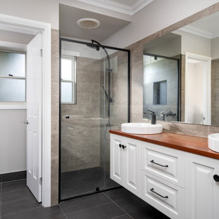Photo of a large transitional 3/4 bathroom in Other with raised-panel cabinets, white cabinets, an alcove shower, gray tile, grey walls, a vessel sink, wood benchtops, black floor, a hinged shower door, brown benchtops, a double vanity and a floating vanity.