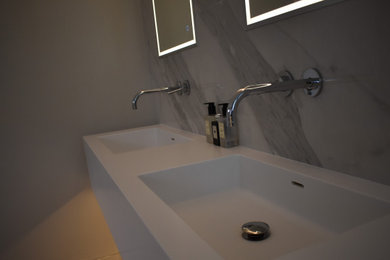 Photo of a large modern ensuite wet room bathroom in Hertfordshire with white cabinets, porcelain tiles, a wall-mounted sink, solid surface worktops, an open shower and white worktops.