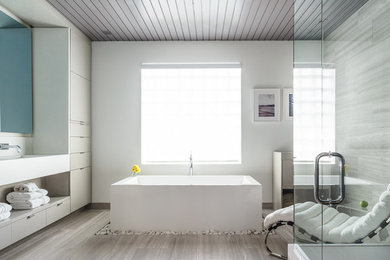 Foto de cuarto de baño principal contemporáneo grande con lavabo integrado, armarios con paneles lisos, puertas de armario grises, bañera exenta, paredes blancas y baldosas y/o azulejos de piedra