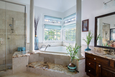 Medium sized mediterranean ensuite bathroom in Philadelphia with raised-panel cabinets, dark wood cabinets, a corner bath, a corner shower, beige tiles, stone tiles, white walls, slate flooring, a submerged sink, marble worktops, beige floors, a hinged door and brown worktops.