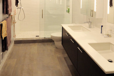Mid-sized trendy master gray tile and porcelain tile porcelain tile double shower photo in New York with an integrated sink, flat-panel cabinets, dark wood cabinets, solid surface countertops, a one-piece toilet and white walls