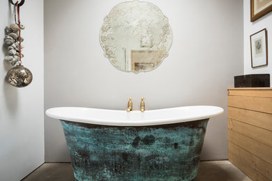 Cette photo montre une salle de bain principale nature de taille moyenne avec une baignoire indépendante, un placard à porte plane, des portes de placard beiges, un mur gris, sol en béton ciré et un sol gris.