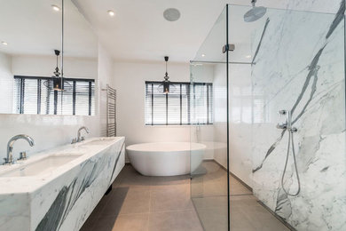 This is an example of a large contemporary ensuite bathroom in London with a freestanding bath, a walk-in shower, a wall mounted toilet, black and white tiles, stone slabs, white walls, porcelain flooring and a submerged sink.