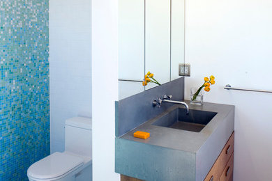 ニューヨークにあるお手頃価格の中くらいなモダンスタイルのおしゃれなマスターバスルーム (フラットパネル扉のキャビネット、中間色木目調キャビネット、ドロップイン型浴槽、シャワー付き浴槽	、青いタイル、ガラスタイル、磁器タイルの床、一体型シンク、コンクリートの洗面台、一体型トイレ	) の写真