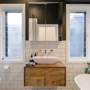 Photo of a contemporary 3/4 bathroom in Sydney with flat-panel cabinets, brown cabinets, a freestanding tub, an alcove shower, a wall-mount toilet, white tile, black walls, a vessel sink, wood benchtops, brown benchtops and a single vanity.