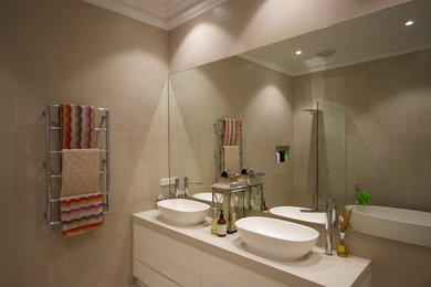 Photo of a medium sized contemporary ensuite bathroom in Melbourne with flat-panel cabinets, white cabinets, white tiles, laminate worktops, a built-in bath, an alcove shower, a two-piece toilet, ceramic tiles, beige walls, ceramic flooring, a vessel sink, beige floors and a hinged door.