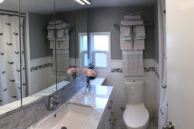ニューヨークにある小さなビーチスタイルのおしゃれなマスターバスルーム (シェーカースタイル扉のキャビネット、白いキャビネット、アルコーブ型浴槽、シャワー付き浴槽	、一体型トイレ	、白いタイル、セラミックタイル、グレーの壁、モザイクタイル、アンダーカウンター洗面器、大理石の洗面台、グレーの床、シャワーカーテン) の写真
