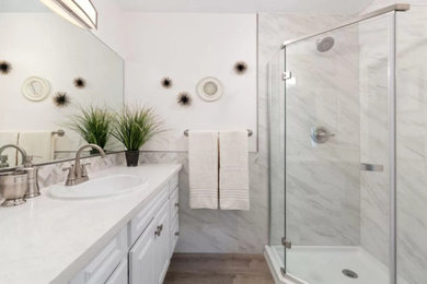 На фото: ванная комната среднего размера в современном стиле с фасадами с выступающей филенкой, белыми фасадами, угловым душем, унитазом-моноблоком, разноцветной плиткой, керамогранитной плиткой, розовыми стенами, полом из ламината, душевой кабиной, накладной раковиной, столешницей из кварцита, коричневым полом, душем с распашными дверями, белой столешницей, тумбой под одну раковину и напольной тумбой