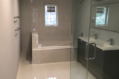 Imagen de cuarto de baño principal grande con puertas de armario de madera en tonos medios, bañera esquinera, ducha esquinera, baldosas y/o azulejos blancos, suelo blanco y encimeras blancas