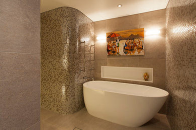 Свежая идея для дизайна: большая главная ванная комната в стиле модернизм с фасадами островного типа, светлыми деревянными фасадами, отдельно стоящей ванной, угловым душем, унитазом-моноблоком, бежевой плиткой, плиткой мозаикой, бежевыми стенами, полом из цементной плитки, настольной раковиной, столешницей из искусственного камня, серым полом, душем с распашными дверями, белой столешницей, акцентной стеной, тумбой под одну раковину, встроенной тумбой и кессонным потолком - отличное фото интерьера