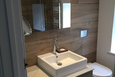 Inspiration for a medium sized modern ensuite bathroom in Dorset with a vessel sink, beige cabinets, a wall mounted toilet, beige tiles, porcelain tiles and porcelain flooring.