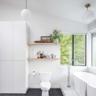 Foto på ett stort funkis badrum för barn, med släta luckor, beige skåp, ett fristående badkar, en öppen dusch, en toalettstol med separat cisternkåpa, vit kakel, marmorkakel, vita väggar, cementgolv, ett fristående handfat, svart golv och med dusch som är öppen
