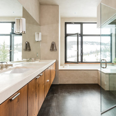 Example of a large trendy master white tile concrete floor bathroom design in Other with flat-panel cabinets, medium tone wood cabinets, beige walls, an undermount sink and solid surface countertops