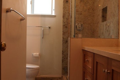 Example of a mid-sized multicolored tile multicolored floor alcove shower design in San Francisco with shaker cabinets, medium tone wood cabinets, a two-piece toilet, white walls, an undermount sink, marble countertops, a hinged shower door and beige countertops