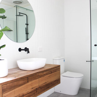 This is an example of a large contemporary 3/4 bathroom in Perth with furniture-like cabinets, medium wood cabinets, a freestanding tub, a corner shower, a one-piece toilet, white tile, subway tile, white walls, porcelain floors, a vessel sink, wood benchtops, grey floor, a hinged shower door, multi-coloured benchtops, a single vanity and a floating vanity.