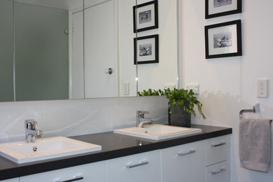 Diseño de cuarto de baño actual con puertas de armario blancas y encimera de cuarzo compacto