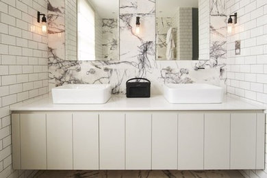 Diseño de cuarto de baño actual con armarios con paneles lisos, puertas de armario grises, paredes blancas, lavabo sobreencimera, suelo multicolor y encimeras blancas