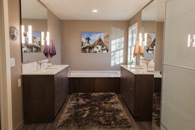 Photo of a large classic ensuite bathroom in Wichita with flat-panel cabinets, dark wood cabinets, an alcove bath, an alcove shower, a two-piece toilet, beige walls, laminate floors, a submerged sink, quartz worktops, brown floors and a hinged door.