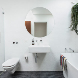 Contemporary master bathroom in Sydney with a freestanding tub, a curbless shower, white tile, white walls, a wall-mount sink, black floor, a single vanity and wood walls.