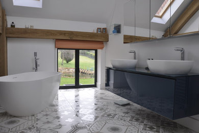 This is an example of a large contemporary ensuite bathroom in Berkshire with glass-front cabinets, blue cabinets, a freestanding bath, a double shower, a wall mounted toilet, white tiles, porcelain tiles, white walls, ceramic flooring, a vessel sink and glass worktops.
