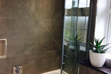 Small contemporary family bathroom in Surrey with a built-in bath, a shower/bath combination, a wall mounted toilet, grey tiles, porcelain tiles, porcelain flooring, marble worktops and a hinged door.