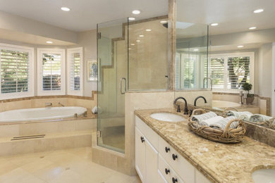 オレンジカウンティにある高級な中くらいなトラディショナルスタイルのおしゃれなマスターバスルーム (落し込みパネル扉のキャビネット、白いキャビネット、アンダーマウント型浴槽、コーナー設置型シャワー、分離型トイレ、茶色いタイル、ライムストーンタイル、ベージュの壁、ライムストーンの床、アンダーカウンター洗面器、ライムストーンの洗面台、ベージュの床、開き戸のシャワー、ブラウンの洗面カウンター、洗面台2つ) の写真