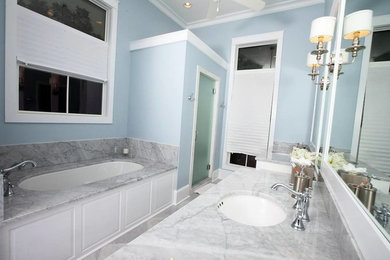 ニューオリンズにあるビーチスタイルのおしゃれなマスターバスルーム (アンダーカウンター洗面器、白いキャビネット、大理石の洗面台、アンダーマウント型浴槽、アルコーブ型シャワー、白いタイル、石タイル、青い壁、大理石の床) の写真