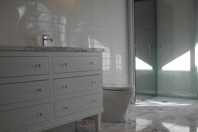 Photo of a medium sized contemporary family bathroom in Calgary with freestanding cabinets, white cabinets, a freestanding bath, a built-in shower, a one-piece toilet, white tiles, ceramic tiles, grey walls, marble flooring, a submerged sink and marble worktops.