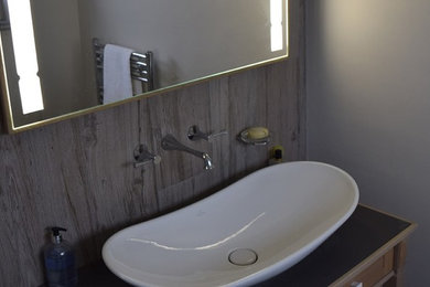 Modelo de cuarto de baño principal tradicional con lavabo tipo consola, puertas de armario beige, encimera de granito, sanitario de pared, baldosas y/o azulejos grises, baldosas y/o azulejos de cerámica, paredes grises y suelo de madera en tonos medios
