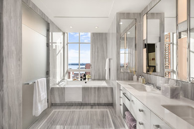 Modern inredning av ett stort vit vitt en-suite badrum, med släta luckor, vita skåp, ett badkar i en alkov, grå kakel, grå väggar, klinkergolv i porslin, ett undermonterad handfat, bänkskiva i akrylsten och grått golv