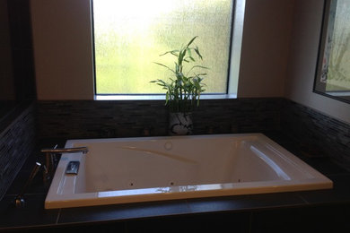 Example of a master multicolored tile and glass tile drop-in bathtub design in Los Angeles with beige walls