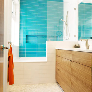 Immagine di una stanza da bagno per bambini moderna con ante lisce, vasca ad alcova, vasca/doccia, piastrelle blu, pavimento con piastrelle di ciottoli e ante in legno chiaro