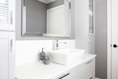 Example of a mid-sized transitional 3/4 porcelain tile and brown floor bathroom design in Toronto with raised-panel cabinets, white cabinets, a two-piece toilet, gray walls, a vessel sink, quartzite countertops and white countertops