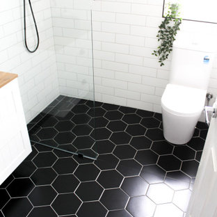 Photo of a small modern kids bathroom in Perth with shaker cabinets, white cabinets, an open shower, a one-piece toilet, white tile, ceramic tile, white walls, porcelain floors, a vessel sink, wood benchtops, black floor, an open shower, beige benchtops, a single vanity, a floating vanity and brick walls.