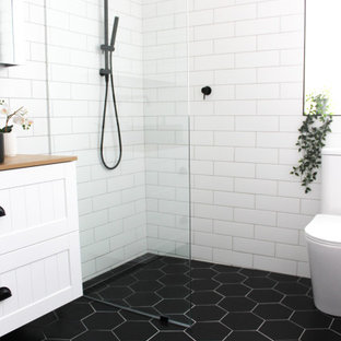 This is an example of a small modern kids bathroom in Perth with shaker cabinets, white cabinets, an open shower, a one-piece toilet, white tile, ceramic tile, white walls, porcelain floors, a vessel sink, wood benchtops, black floor, an open shower, beige benchtops, a single vanity, a floating vanity and brick walls.