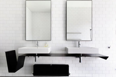 Modern inredning av ett mellanstort badrum, med vit kakel, tunnelbanekakel, svarta skåp, ett platsbyggt badkar, en vägghängd toalettstol, vita väggar, klinkergolv i keramik, ett väggmonterat handfat och bänkskiva i rostfritt stål
