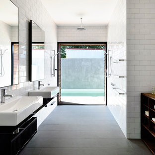 Immagine di una stanza da bagno minimal di medie dimensioni con lavabo sospeso, piastrelle bianche, piastrelle diamantate, nessun'anta, ante nere, pareti bianche, pavimento con piastrelle in ceramica, top in acciaio inossidabile, doccia a filo pavimento e pavimento grigio