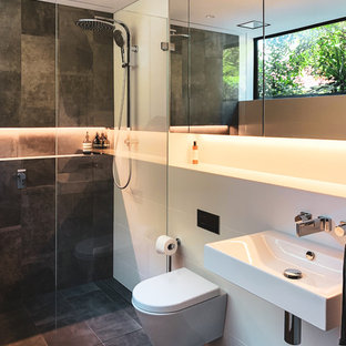 This is an example of a contemporary bathroom in Sydney with a curbless shower, a wall-mount toilet, gray tile, white tile, white walls, a wall-mount sink, grey floor and an open shower.