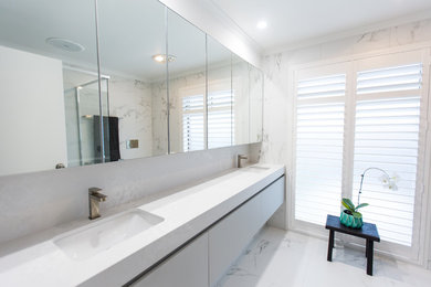 Inredning av ett modernt mellanstort badrum, med vita skåp, ett fristående badkar, en hörndusch, porslinskakel, vita väggar, klinkergolv i porslin, bänkskiva i akrylsten, vitt golv och dusch med gångjärnsdörr