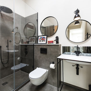 Medium sized industrial bathroom in London with a wall mounted toilet, grey tiles, white walls, a console sink, black floors and a sliding door.