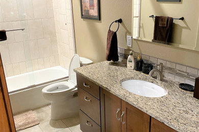 This is an example of a small classic family bathroom in Denver with shaker cabinets, medium wood cabinets, a shower/bath combination, beige tiles, porcelain tiles, beige walls, porcelain flooring, a submerged sink, granite worktops, beige floors, a sliding door and beige worktops.