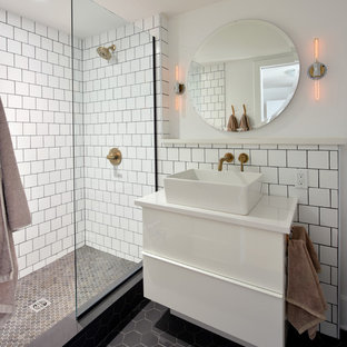 Ejemplo de cuarto de baño con ducha, industrial, de tamaño medio, con armarios con paneles lisos, puertas de armario blancas, ducha abierta, baldosas y/o azulejos blancos, baldosas y/o azulejos de cemento, paredes blancas, lavabo sobreencimera, suelo de baldosas de porcelana, encimera de acrílico, suelo negro, ducha abierta y encimeras blancas