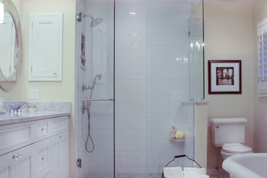 Klassisk inredning av ett vit vitt en-suite badrum, med ett undermonterad handfat, luckor med infälld panel, vita skåp, marmorbänkskiva, ett fristående badkar, en toalettstol med separat cisternkåpa, marmorgolv, vit kakel, keramikplattor, vitt golv och dusch med gångjärnsdörr