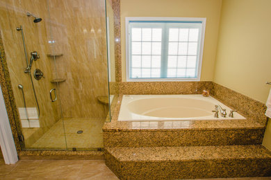 Diseño de cuarto de baño principal actual grande con armarios con paneles con relieve, puertas de armario rojas, ducha esquinera, paredes amarillas, suelo de travertino, lavabo bajoencimera y encimera de granito