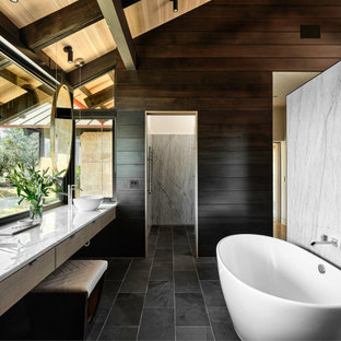 Mid-sized contemporary master bathroom in Austin with flat-panel cabinets, light wood cabinets, a freestanding tub, gray tile, marble, brown walls, slate floors, a vessel sink, quartzite benchtops, black floor, white benchtops, a double vanity, a floating vanity, wood, exposed beam, vaulted and wood walls.