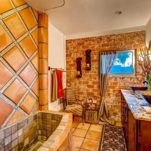 Mittelgroßes Mediterranes Duschbad mit profilierten Schrankfronten, dunklen Holzschränken, Eckbadewanne, Duschbadewanne, braunen Fliesen, Terrakottafliesen, weißer Wandfarbe, Terrakottaboden, Aufsatzwaschbecken, Granit-Waschbecken/Waschtisch, orangem Boden, Duschvorhang-Duschabtrennung und brauner Waschtischplatte in Phoenix