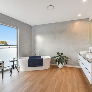 This is an example of a contemporary bathroom in Sunshine Coast with flat-panel cabinets, white cabinets, a freestanding tub, grey walls, medium hardwood floors, a vessel sink, brown floor and grey benchtops.