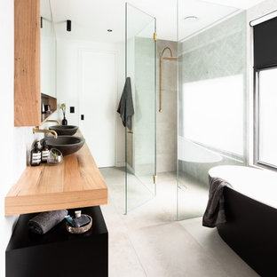 Photo of an industrial bathroom in Melbourne with black cabinets, a freestanding tub, gray tile, white walls, a vessel sink, wood benchtops, grey floor, brown benchtops, a double vanity and a floating vanity.