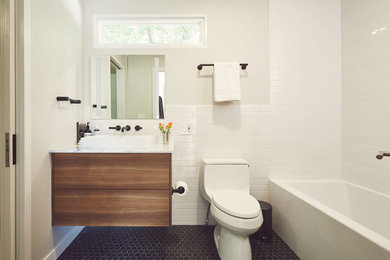 ニューヨークにある高級な小さなコンテンポラリースタイルのおしゃれなマスターバスルーム (フラットパネル扉のキャビネット、茶色いキャビネット、アルコーブ型浴槽、シャワー付き浴槽	、一体型トイレ	、白いタイル、セラミックタイル、グレーの壁、セラミックタイルの床、ベッセル式洗面器、大理石の洗面台、黒い床、シャワーカーテン、白い洗面カウンター) の写真